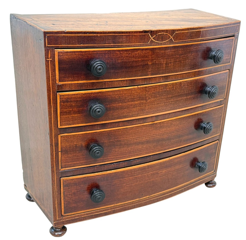 An 18th-century Georgian mahogany miniature bowfront chest of drawers featuring boxwood inlay, four graduated drawers with turned wooden knobs, and low bun feet. View VIII
