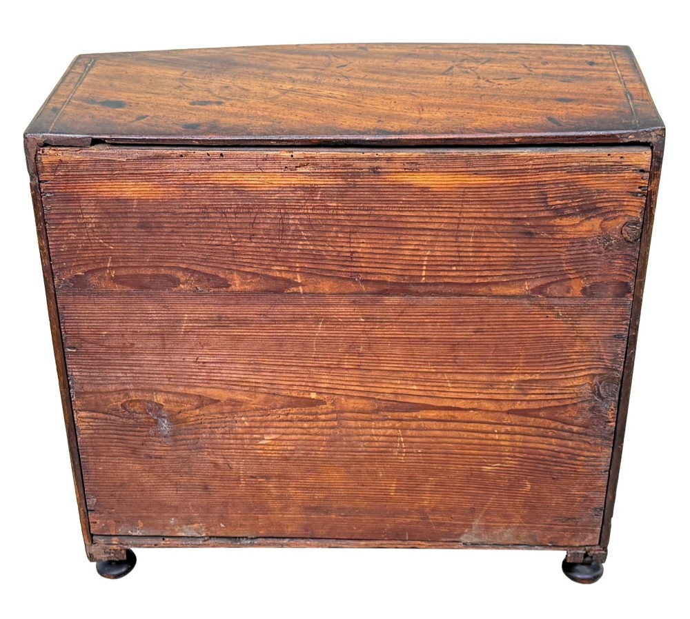 An 18th-century Georgian mahogany miniature bowfront chest of drawers featuring boxwood inlay, four graduated drawers with turned wooden knobs, and low bun feet. View IX