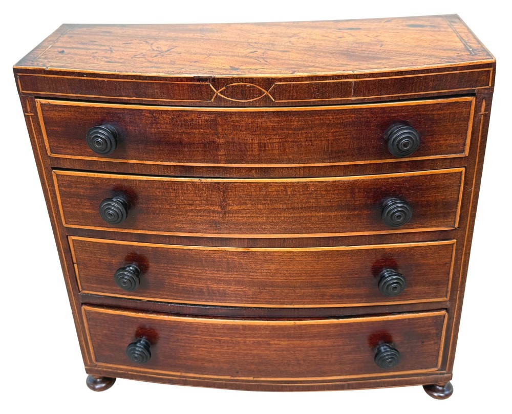 An 18th-century Georgian mahogany miniature bowfront chest of drawers featuring boxwood inlay, four graduated drawers with turned wooden knobs, and low bun feet. View XI
