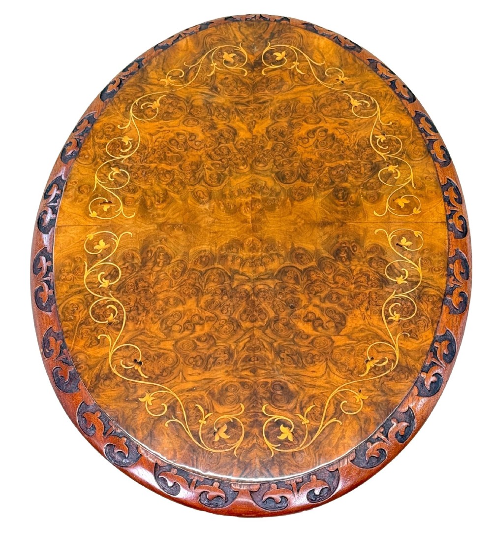 A Victorian burr walnut oval occasional table with marquetry inlay top, a turned central pedestal, and carved tripod cabriole feet. View VI