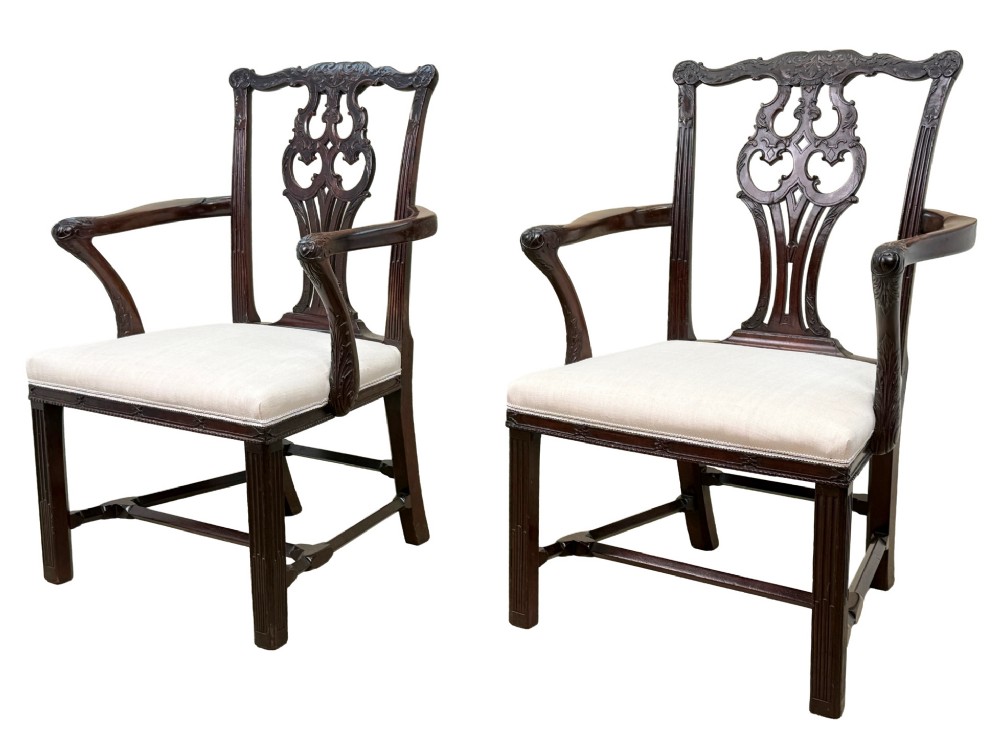 A pair of 18th-century Chippendale mahogany carver armchairs featuring intricately carved pierced back splats, curved arms, and neutral upholstered drop-in seats.