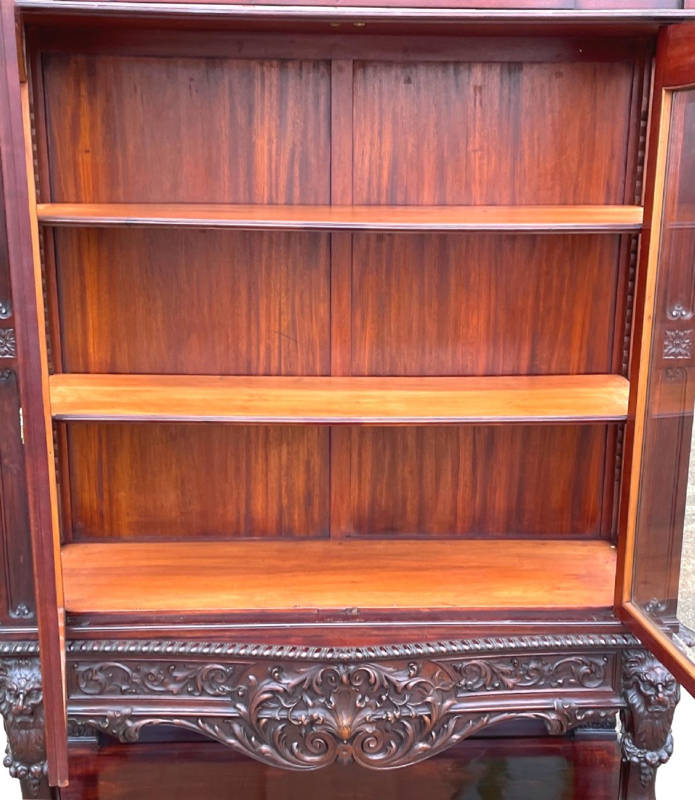 A 19th-century dark mahogany display cabinet featuring a carved crest, glazed doors, and lower support with carved lion mask legs. View VIII