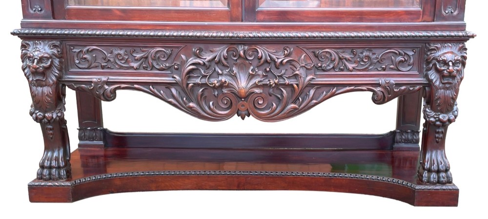 A 19th-century dark mahogany display cabinet featuring a carved crest, glazed doors, and lower support with carved lion mask legs. View XIII