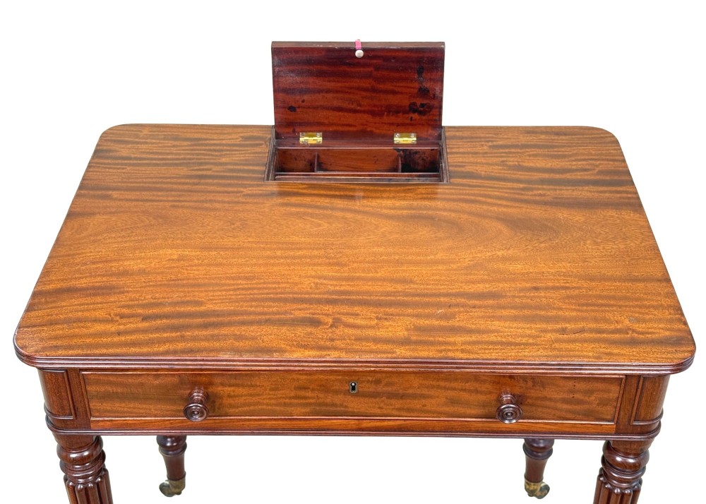A Regency mahogany chamber writing table featuring a single frieze drawer, fluted turned legs on brass castors, and an inset surface hatch. View IV