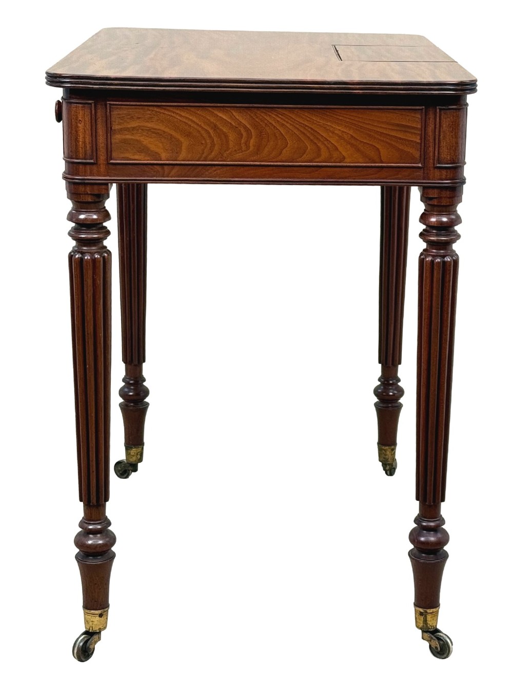 A Regency mahogany chamber writing table featuring a single frieze drawer, fluted turned legs on brass castors, and an inset surface hatch. View VI