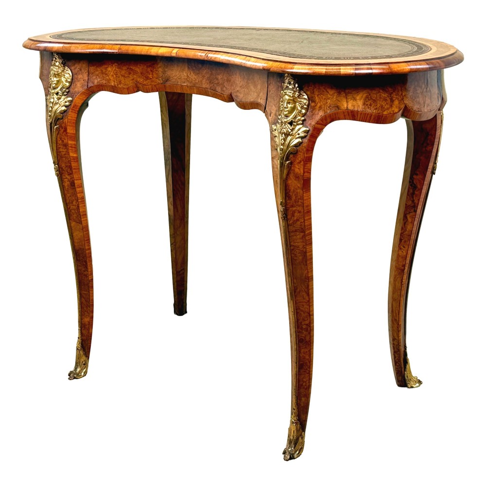 A 19th-century burr walnut kidney-shaped writing table featuring an inset leather top, gilt bronze espagnolette mounts, and cabriole legs.