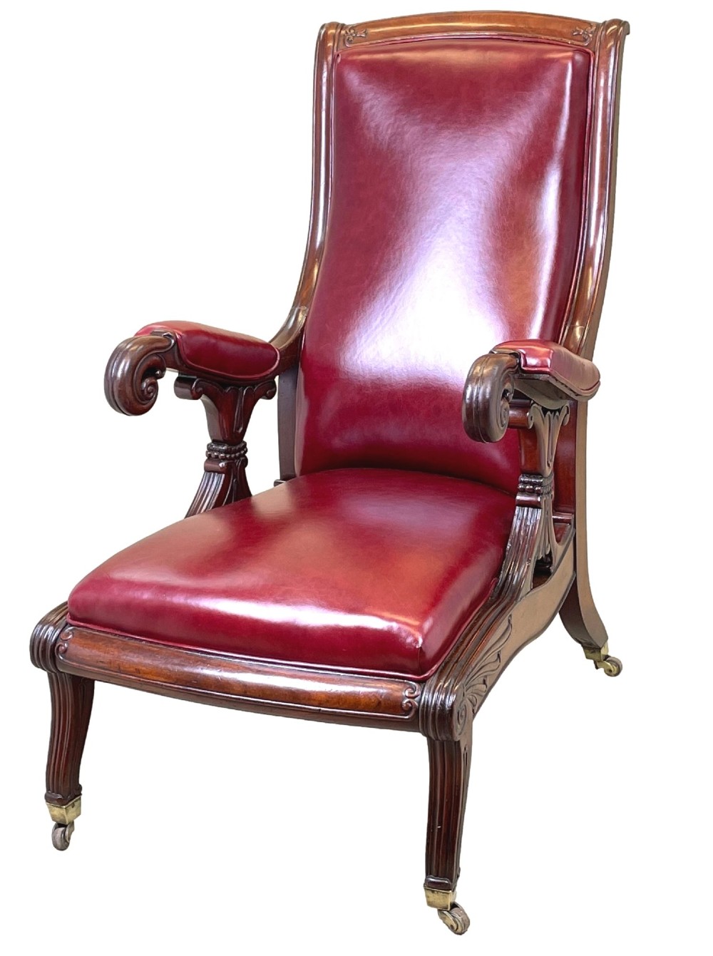A 19th-century high-back mahogany library chair upholstered in deep red leather with carved scroll armrests and brass castors.