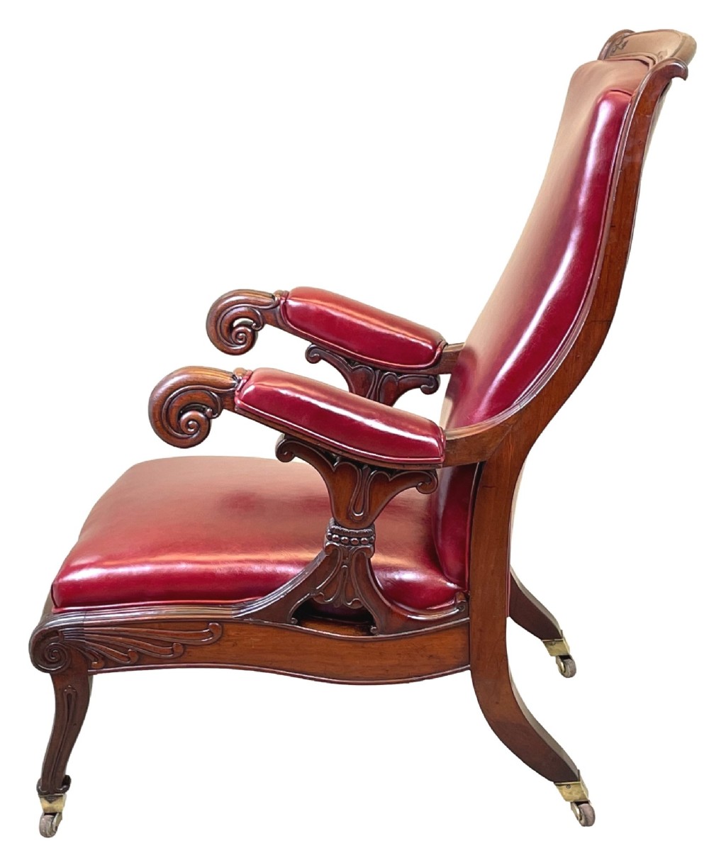 A 19th-century high-back mahogany library chair upholstered in deep red leather with carved scroll armrests and brass castors. View II