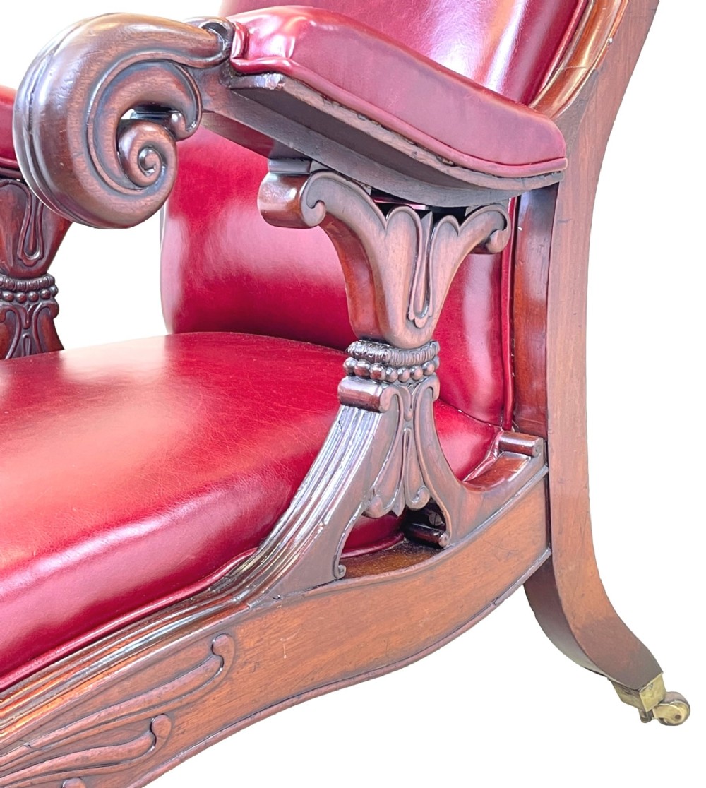 A 19th-century high-back mahogany library chair upholstered in deep red leather with carved scroll armrests and brass castors. View III
