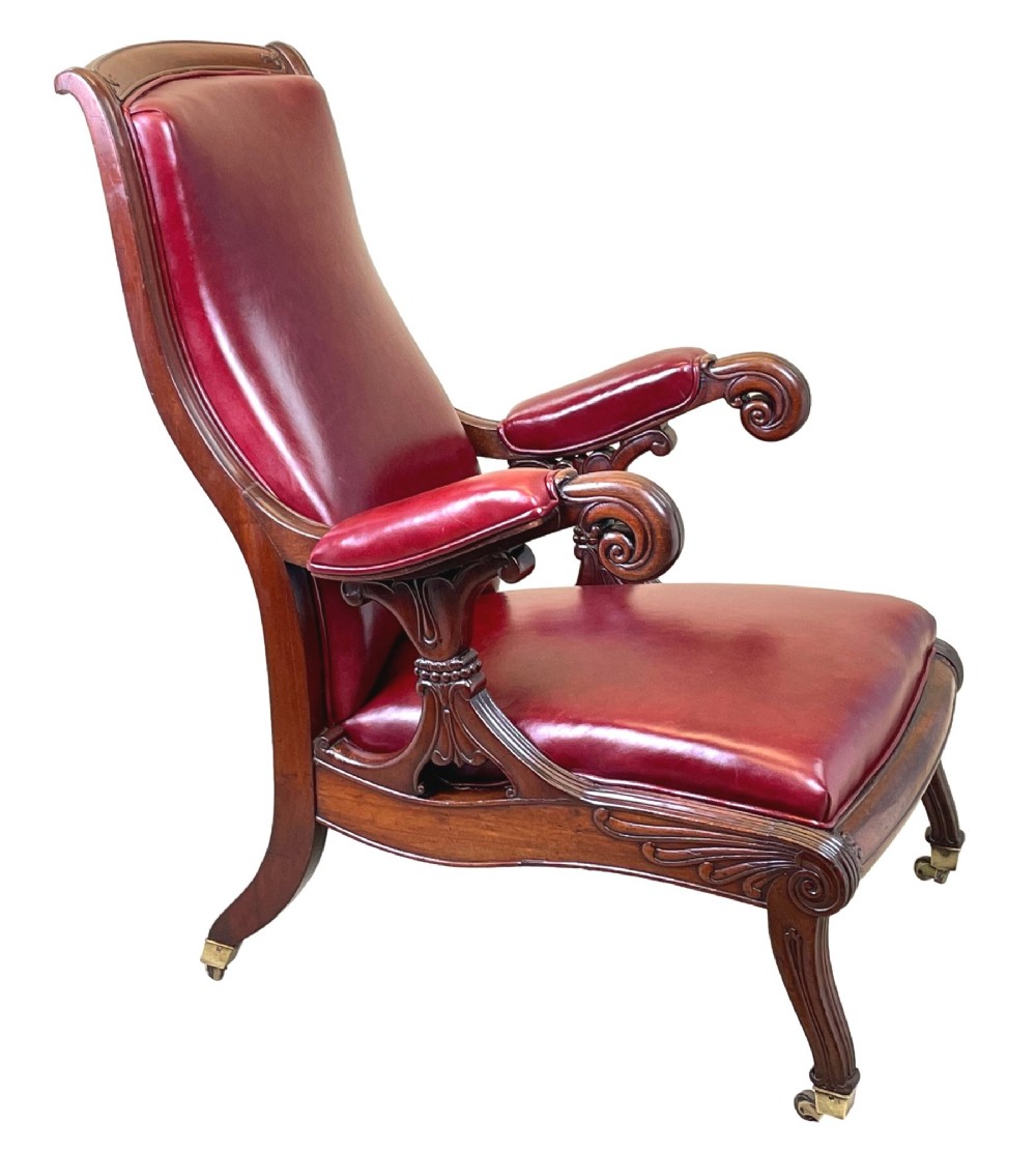 A 19th-century high-back mahogany library chair upholstered in deep red leather with carved scroll armrests and brass castors. View V
