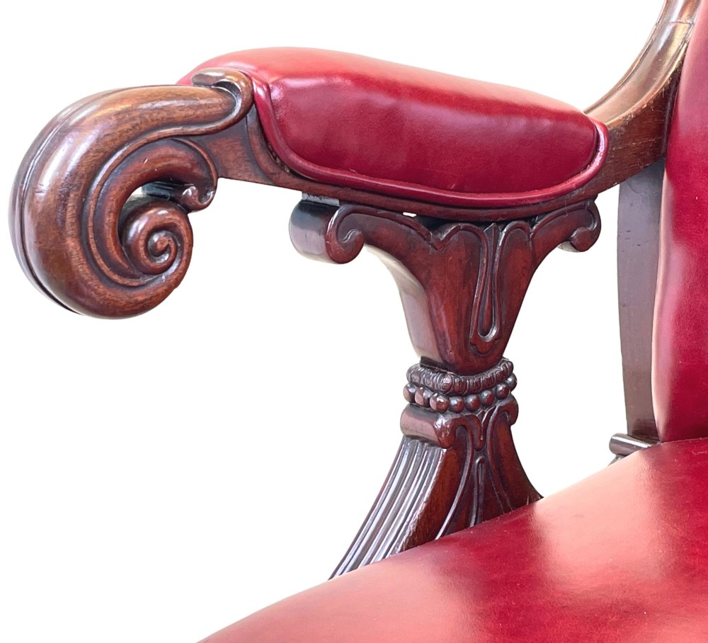 A 19th-century high-back mahogany library chair upholstered in deep red leather with carved scroll armrests and brass castors. View VI