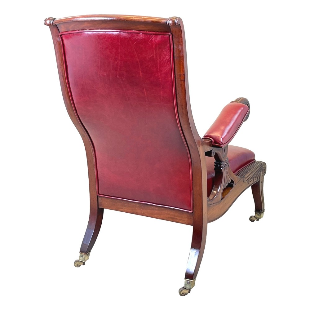 A 19th-century high-back mahogany library chair upholstered in deep red leather with carved scroll armrests and brass castors. View VII