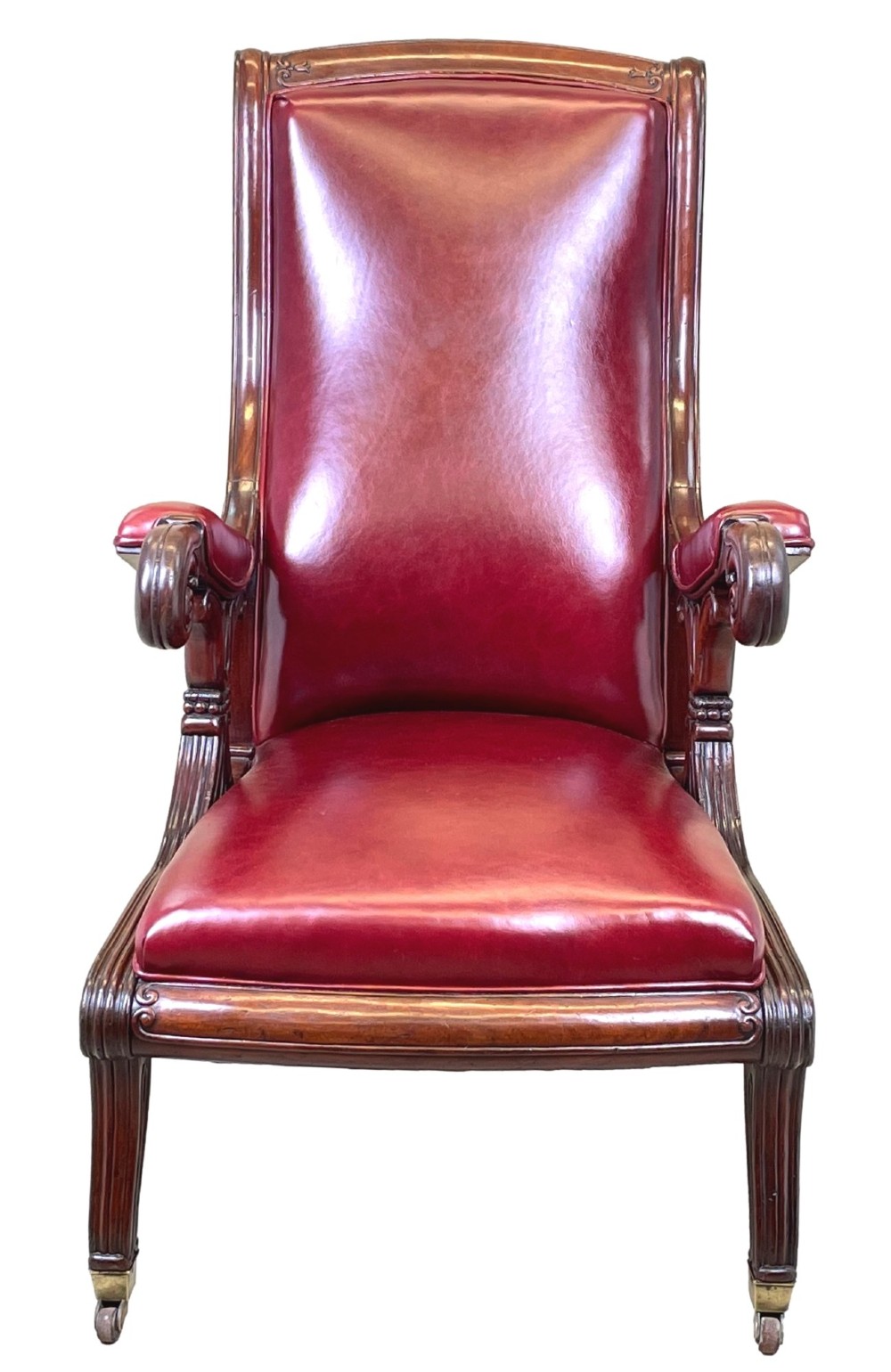 A 19th-century high-back mahogany library chair upholstered in deep red leather with carved scroll armrests and brass castors. View IX
