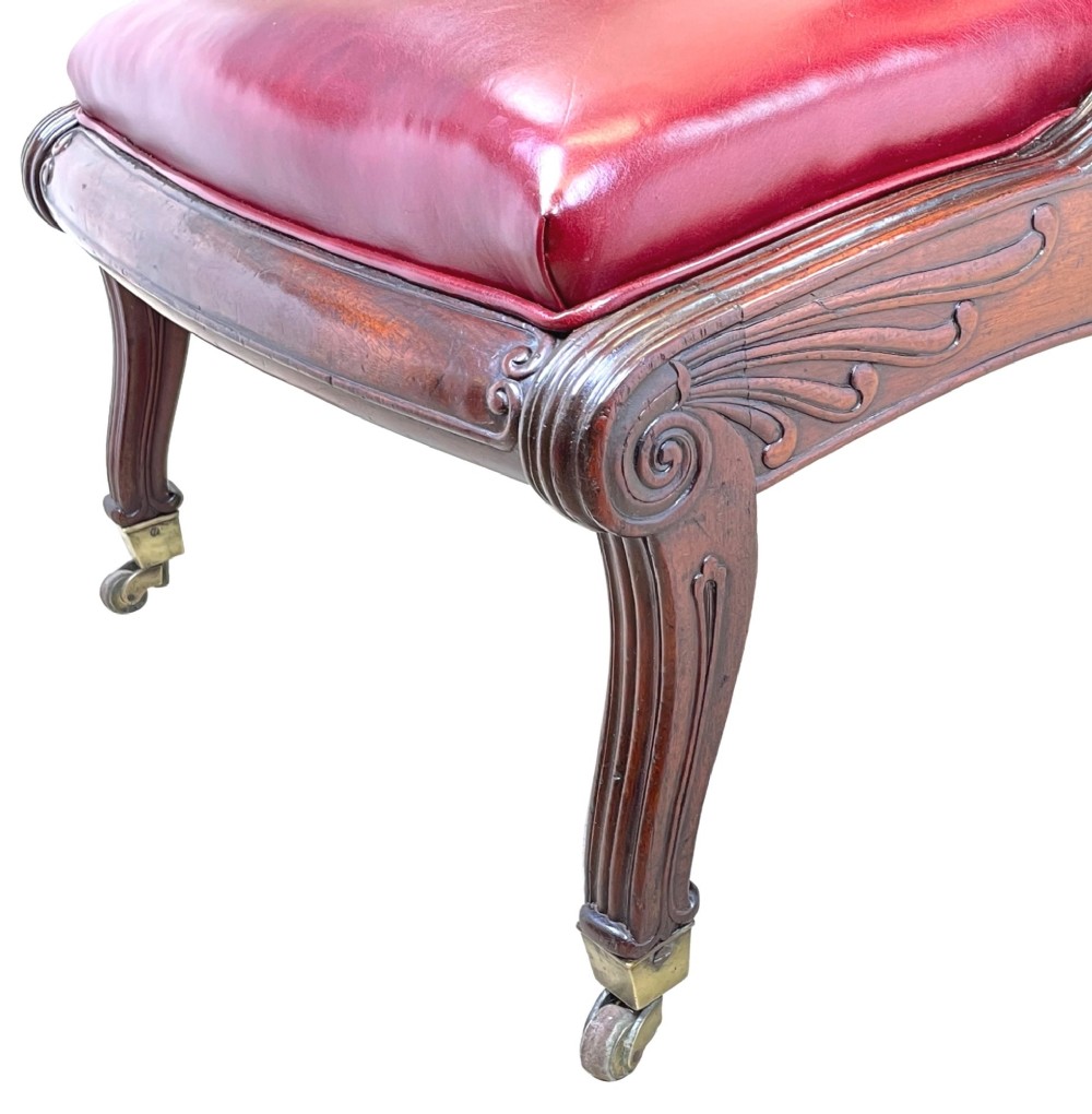 A 19th-century high-back mahogany library chair upholstered in deep red leather with carved scroll armrests and brass castors. View X