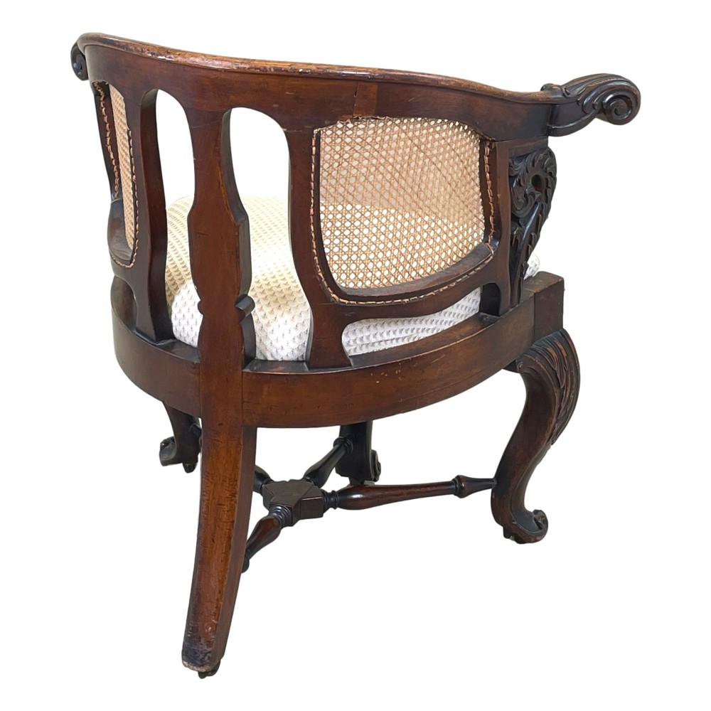 A 19th-century mahogany Burgermeister desk chair featuring a curved backrest with woven cane panels, carved armrests, an upholstered cream seat, and cabriole legs. View XI