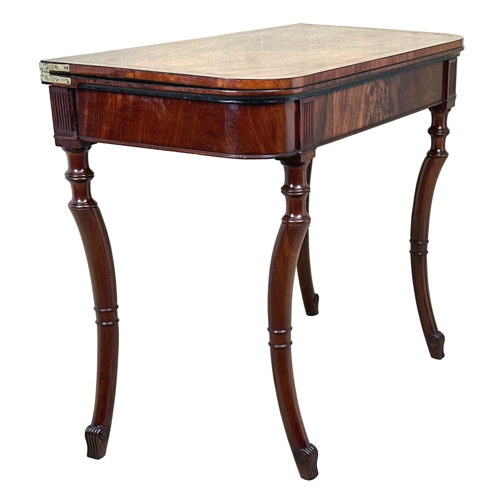 A Regency mahogany fold-over tea table featuring a flame mahogany frieze, reeded corner blocks, and four curved legs with ring-turned detailing. View II