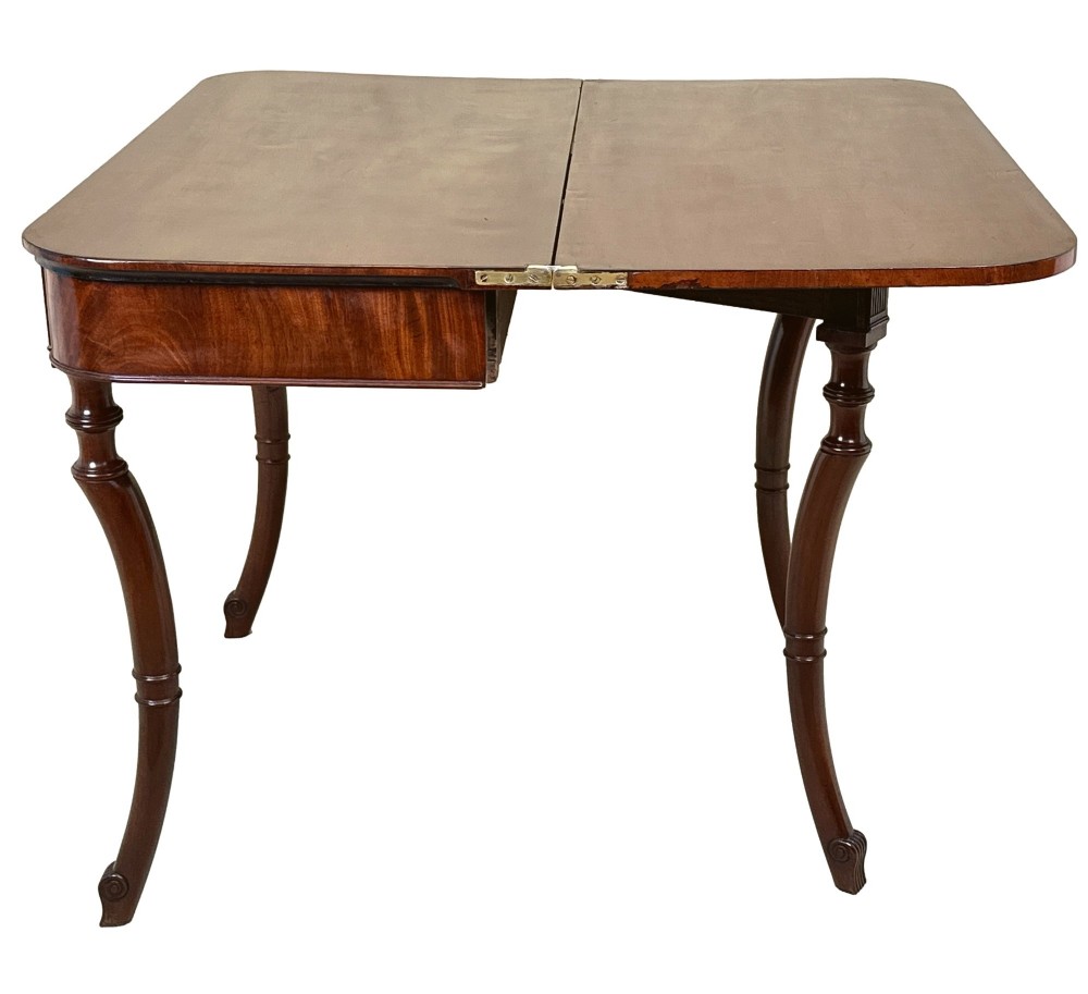 A Regency mahogany fold-over tea table featuring a flame mahogany frieze, reeded corner blocks, and four curved legs with ring-turned detailing. View III