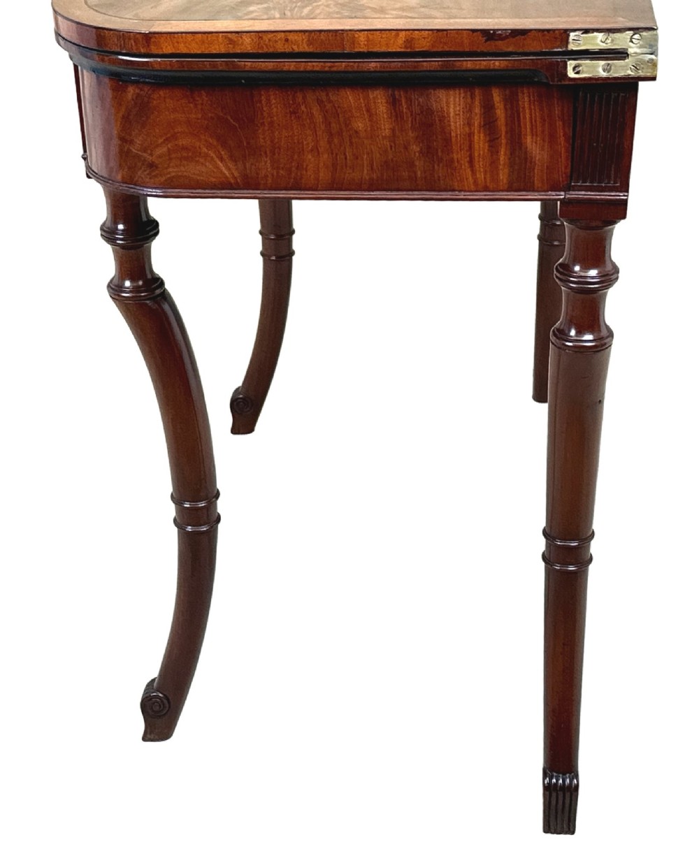 A Regency mahogany fold-over tea table featuring a flame mahogany frieze, reeded corner blocks, and four curved legs with ring-turned detailing. View VIII