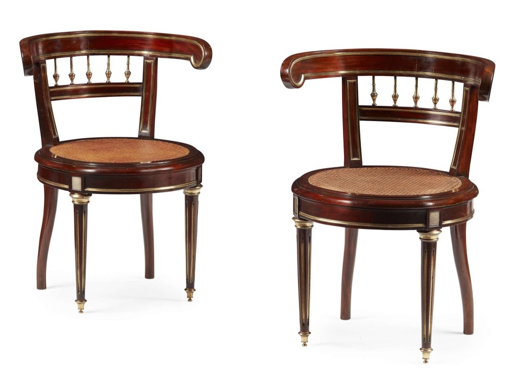 A pair of 19th-century French mahogany curved-back salon chairs with brass mounts, spindle details, woven cane seats, and turned front legs.