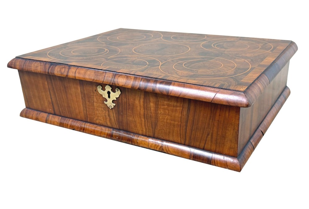 A shallow rectangular William and Mary period wooden box with laburnum oyster veneered patterns, concentric circular stringing on the lid, and a brass keyhole escutcheon on the front panel.