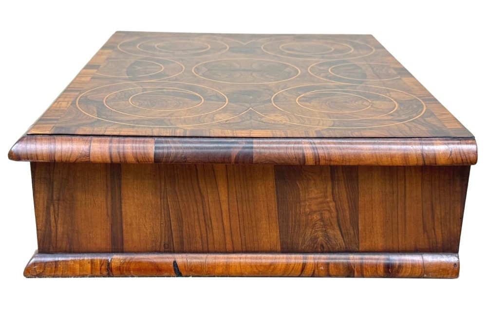 A shallow rectangular William and Mary period wooden box with laburnum oyster veneered patterns, concentric circular stringing on the lid, and a brass keyhole escutcheon on the front panel. View V