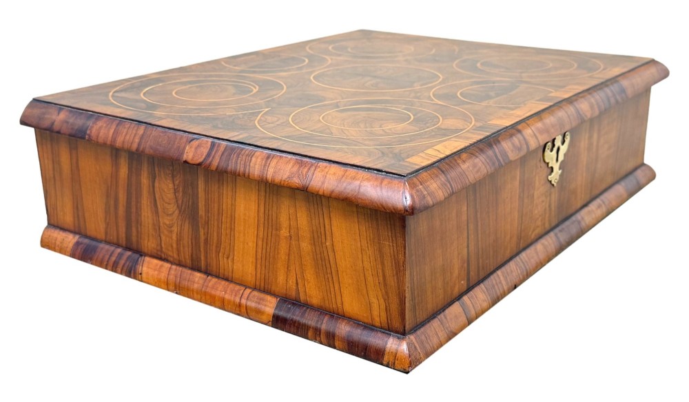 A shallow rectangular William and Mary period wooden box with laburnum oyster veneered patterns, concentric circular stringing on the lid, and a brass keyhole escutcheon on the front panel. View VII