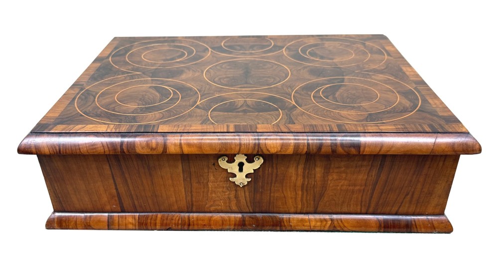 A shallow rectangular William and Mary period wooden box with laburnum oyster veneered patterns, concentric circular stringing on the lid, and a brass keyhole escutcheon on the front panel. View X