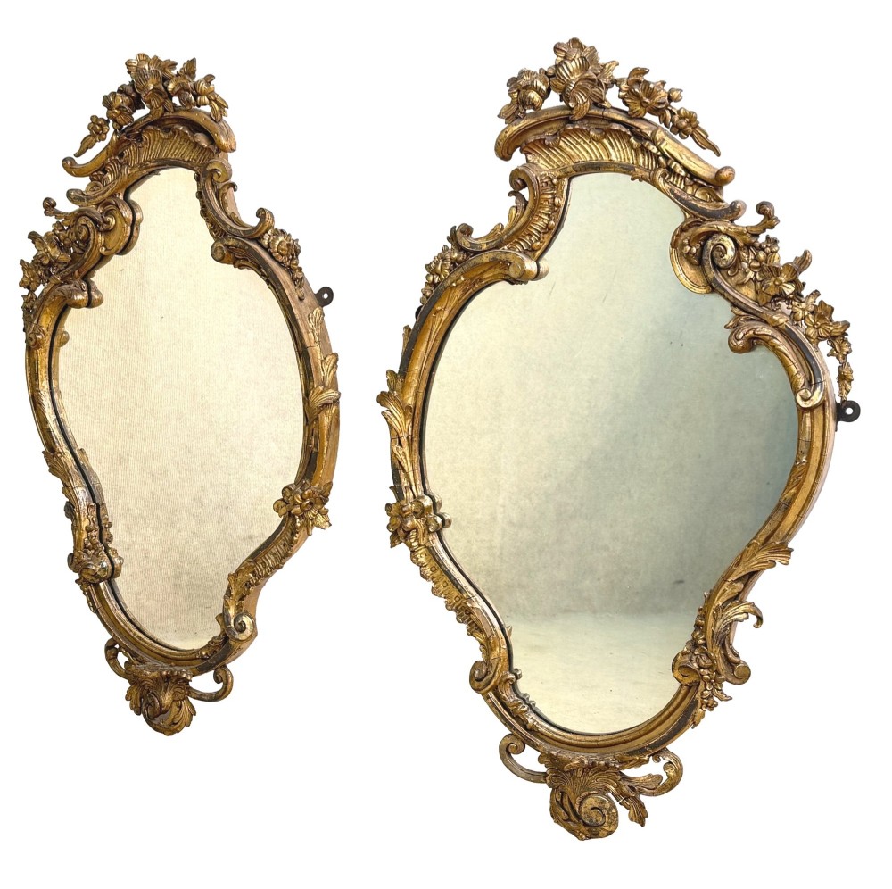 A pair of mid-19th-century cartouche-form wall mirrors featuring ornate carved giltwood and gesso frames decorated with scrolling foliage and floral cresting. View II