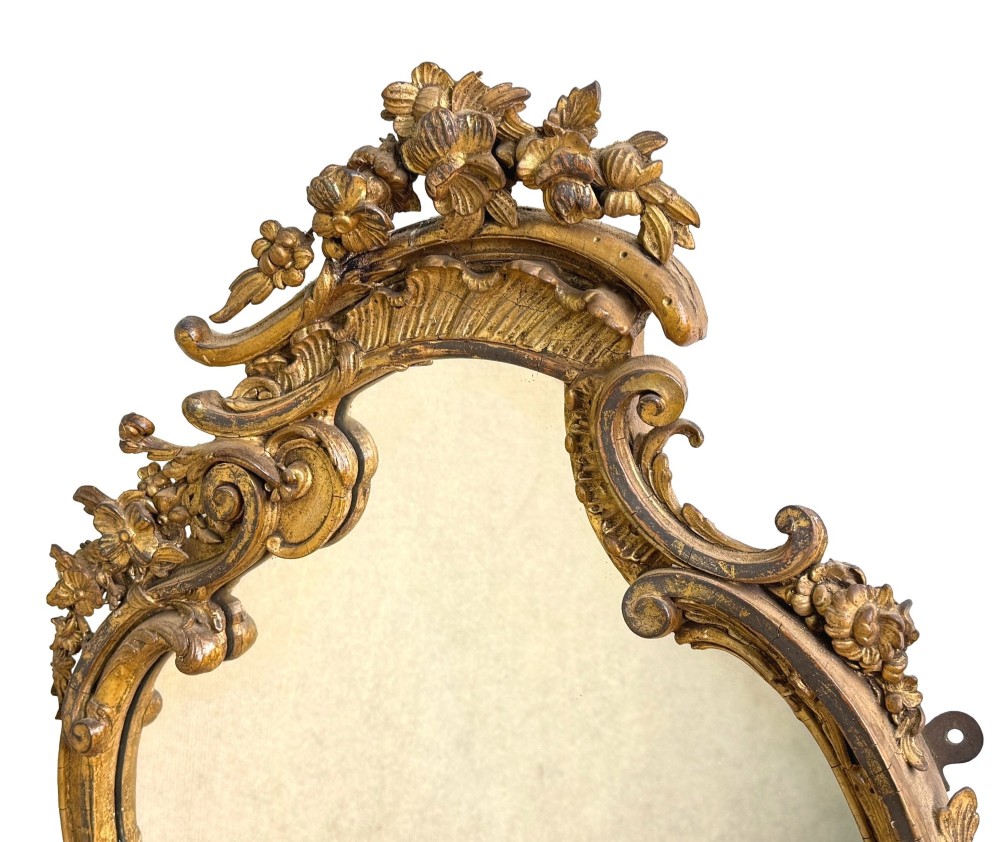 A pair of mid-19th-century cartouche-form wall mirrors featuring ornate carved giltwood and gesso frames decorated with scrolling foliage and floral cresting. View VI