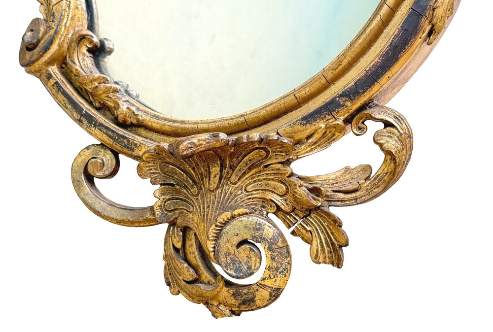 A pair of mid-19th-century cartouche-form wall mirrors featuring ornate carved giltwood and gesso frames decorated with scrolling foliage and floral cresting. View X