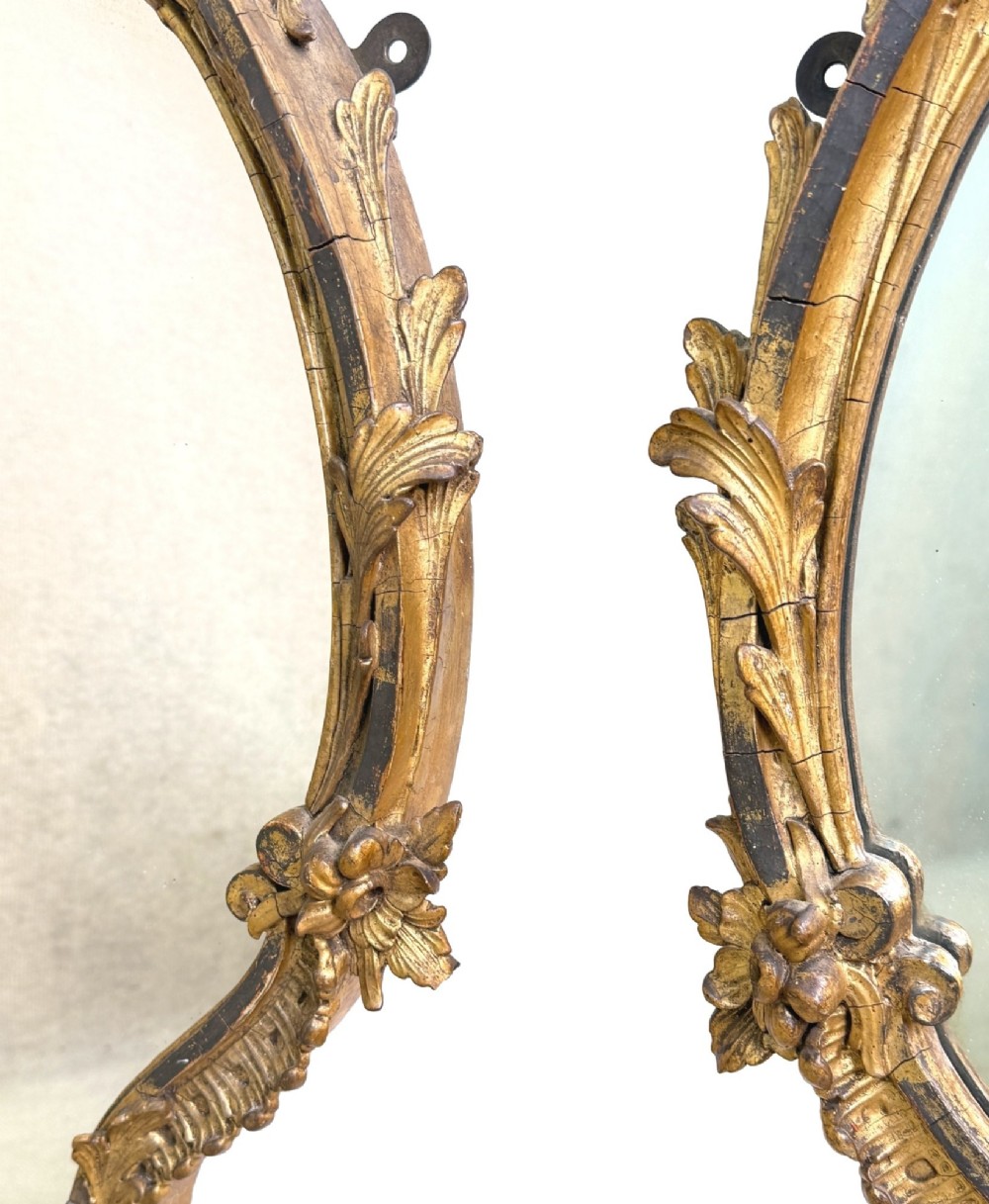 A pair of mid-19th-century cartouche-form wall mirrors featuring ornate carved giltwood and gesso frames decorated with scrolling foliage and floral cresting. View XI