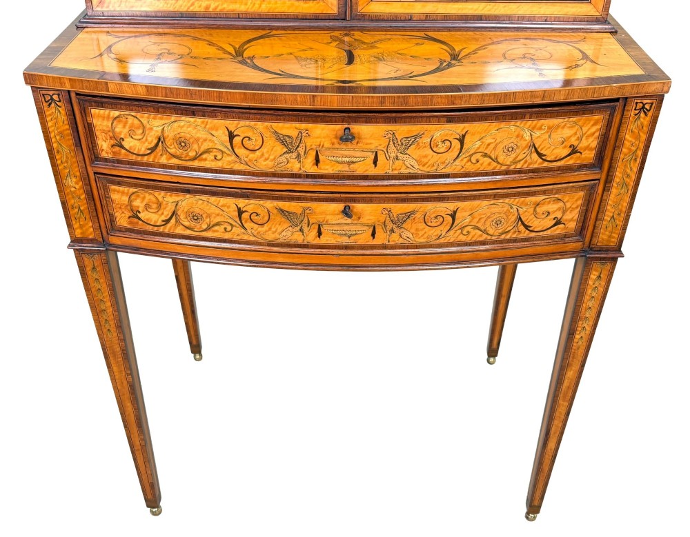A 19th-century inlaid satinwood display cabinet featuring an arched cresting, glazed upper doors, marquetry frieze drawers, and square tapered legs. View VI