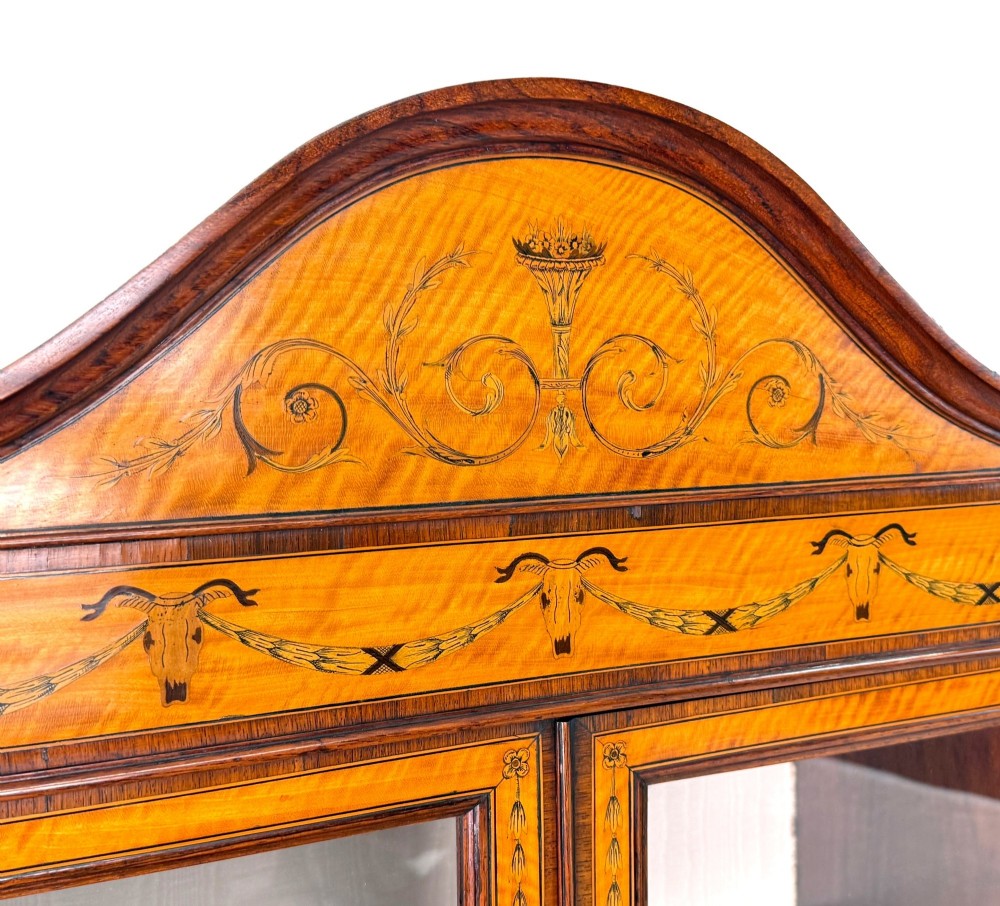 A 19th-century inlaid satinwood display cabinet featuring an arched cresting, glazed upper doors, marquetry frieze drawers, and square tapered legs. View IX