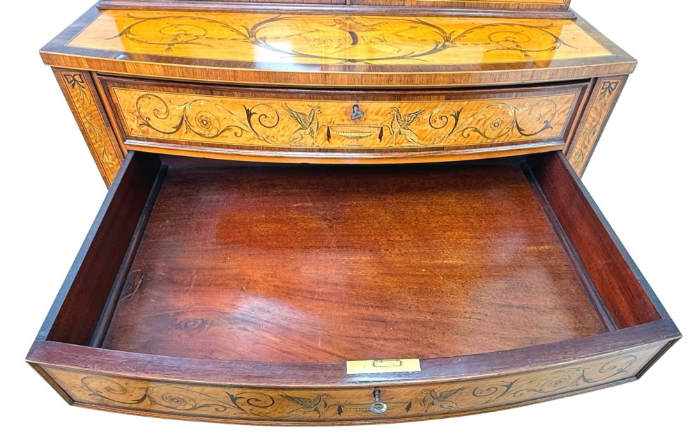 A 19th-century inlaid satinwood display cabinet featuring an arched cresting, glazed upper doors, marquetry frieze drawers, and square tapered legs. View XII