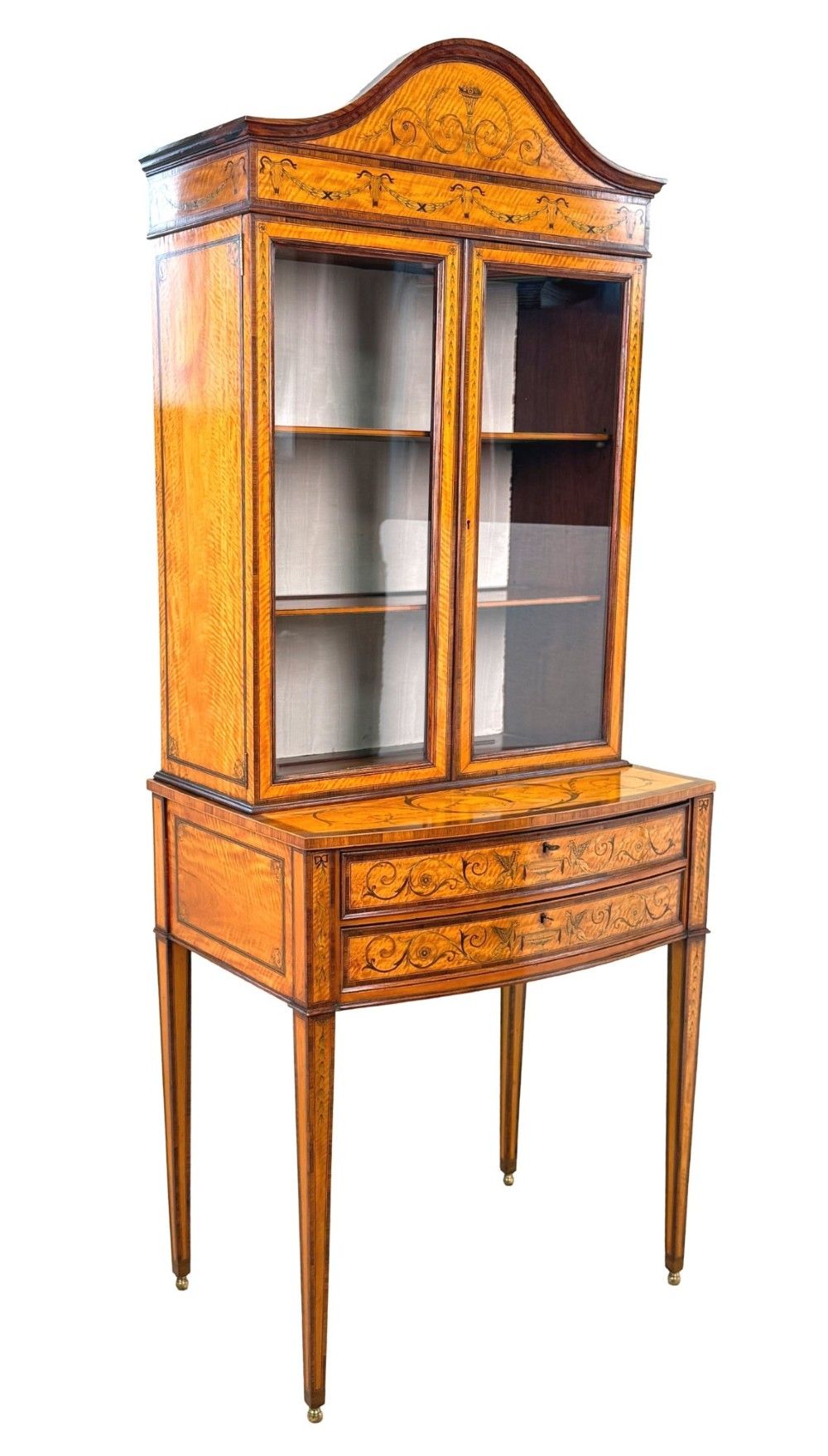 A 19th-century inlaid satinwood display cabinet featuring an arched cresting, glazed upper doors, marquetry frieze drawers, and square tapered legs. View XV