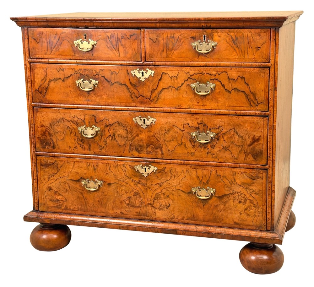 An early eighteenth-century Queen Anne walnut chest of drawers featuring two short over three long graduated drawers, brass handles, pierced escutcheons, and turned bun feet.