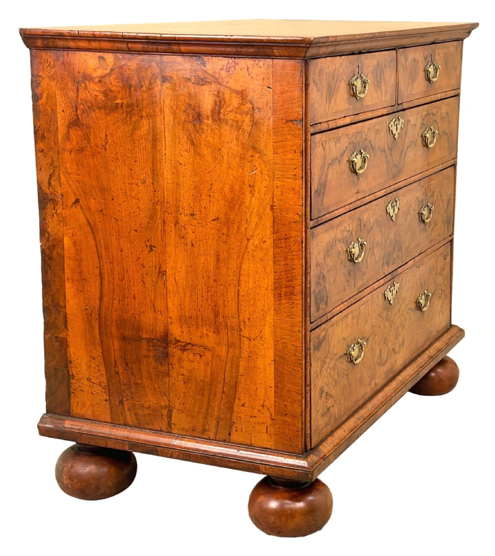 An early eighteenth-century Queen Anne walnut chest of drawers featuring two short over three long graduated drawers, brass handles, pierced escutcheons, and turned bun feet. View II