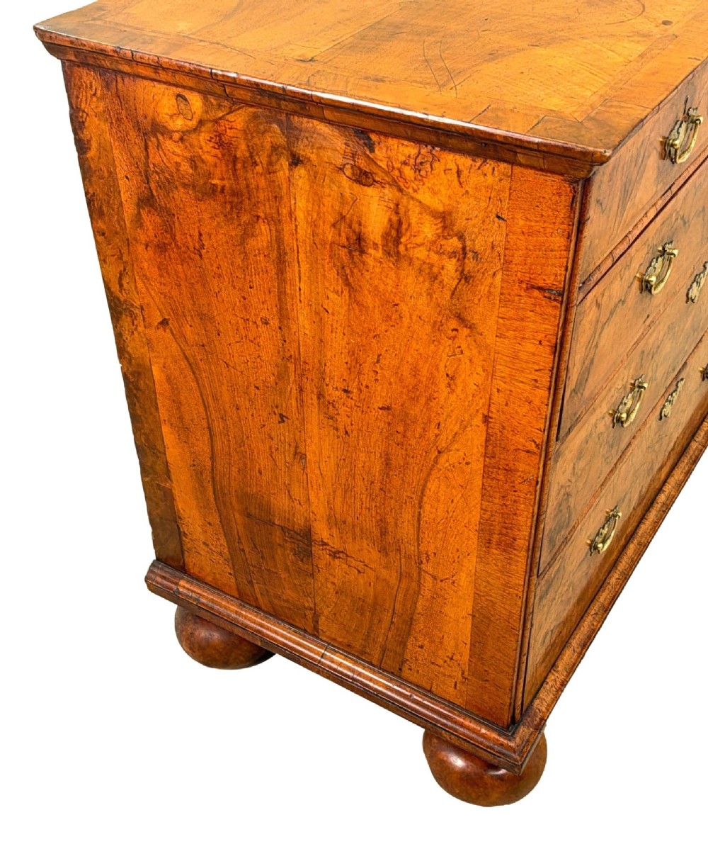 An early eighteenth-century Queen Anne walnut chest of drawers featuring two short over three long graduated drawers, brass handles, pierced escutcheons, and turned bun feet. View IV