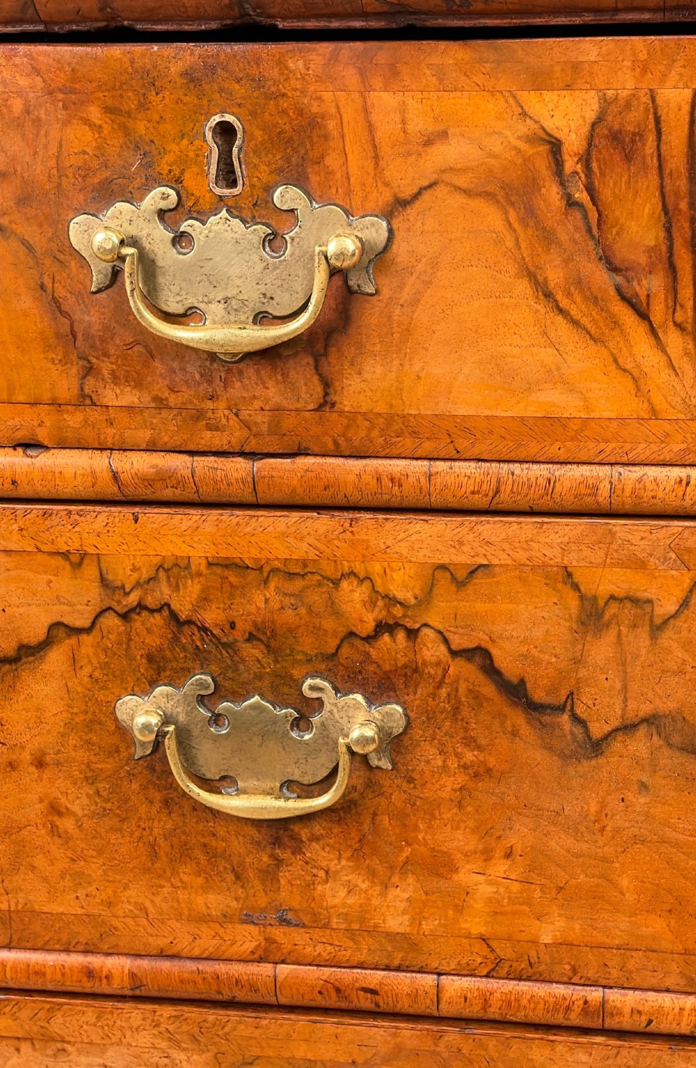An early eighteenth-century Queen Anne walnut chest of drawers featuring two short over three long graduated drawers, brass handles, pierced escutcheons, and turned bun feet. View VII
