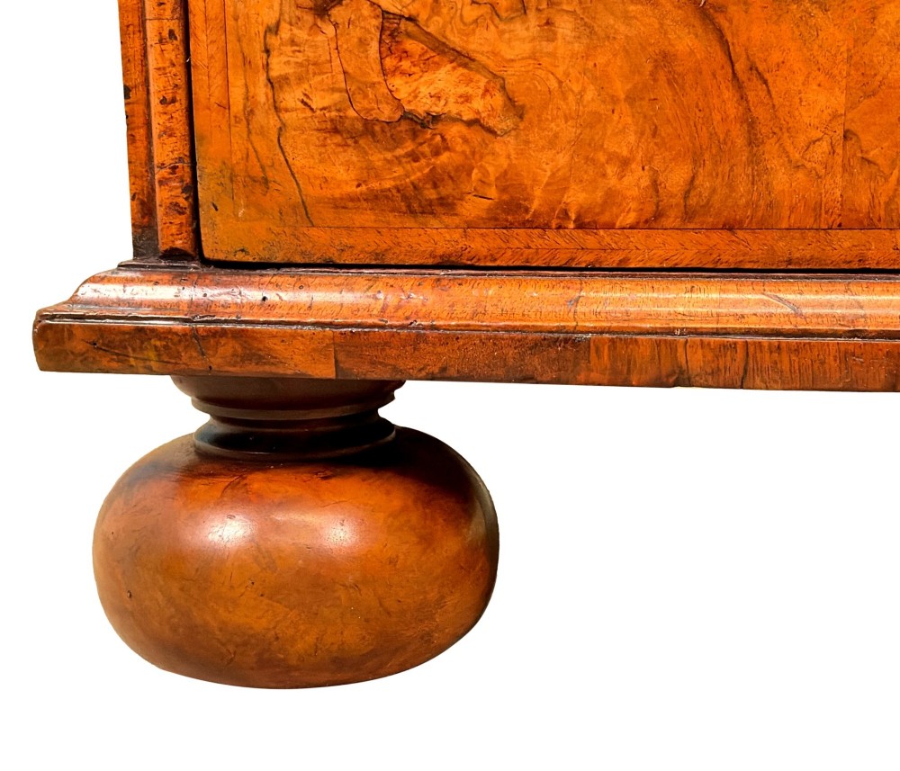 An early eighteenth-century Queen Anne walnut chest of drawers featuring two short over three long graduated drawers, brass handles, pierced escutcheons, and turned bun feet. View XII