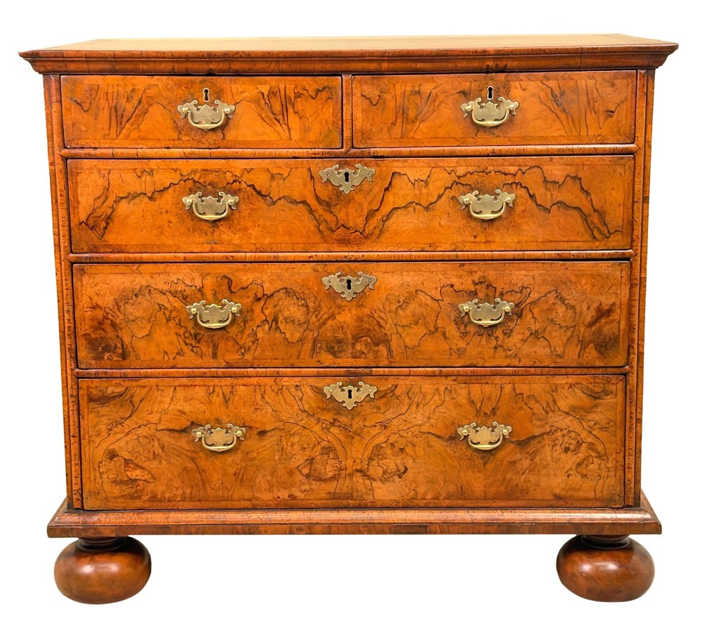 An early eighteenth-century Queen Anne walnut chest of drawers featuring two short over three long graduated drawers, brass handles, pierced escutcheons, and turned bun feet. View XV