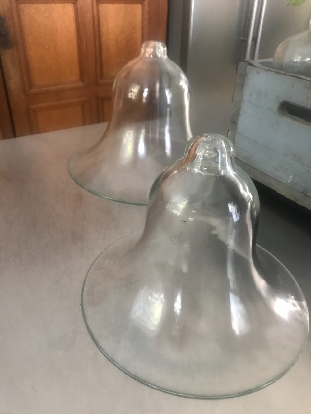 A pair of hand-blown clear glass bell cloches featuring flared rims and knopped handles.