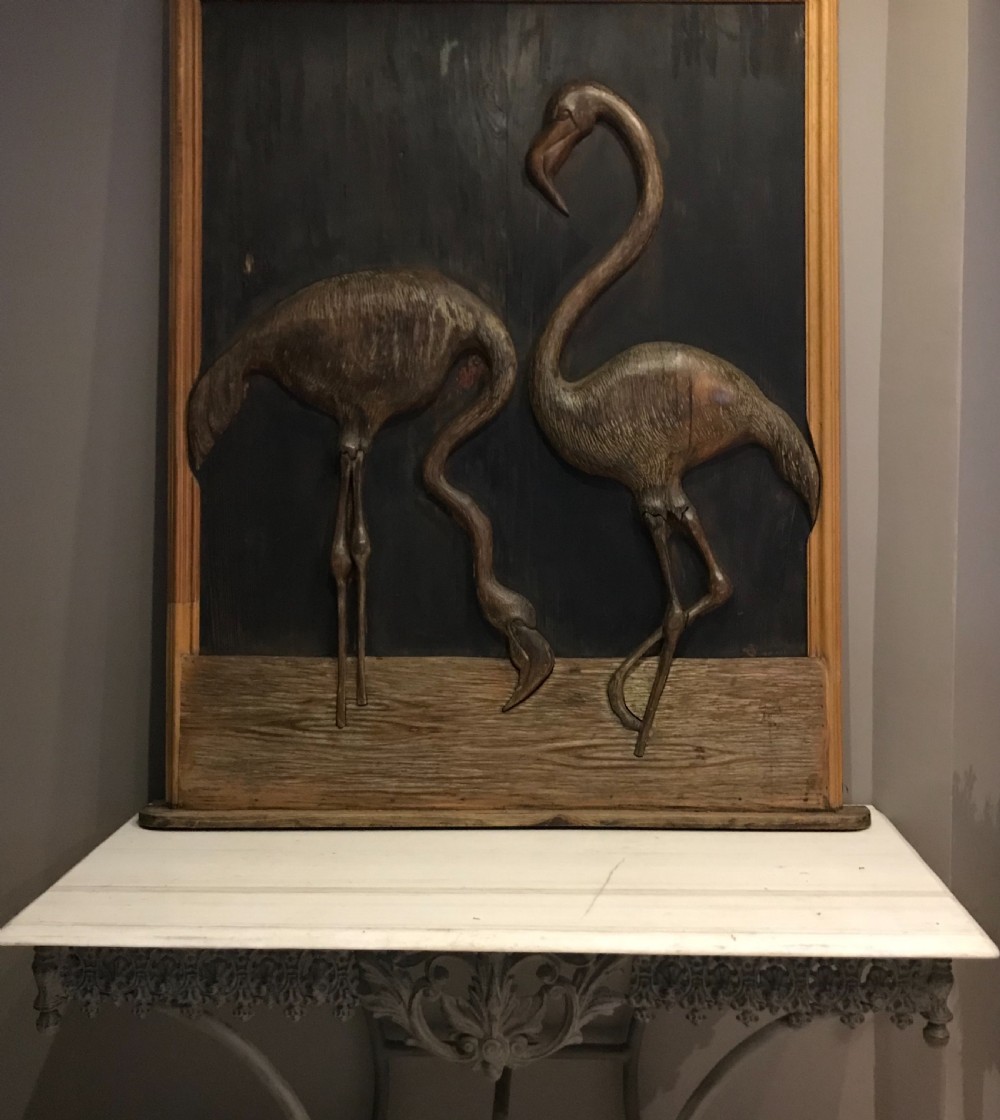 An Arts and Crafts relief carved wooden wall panel depicting two flamingos within a dark painted field and framed border.