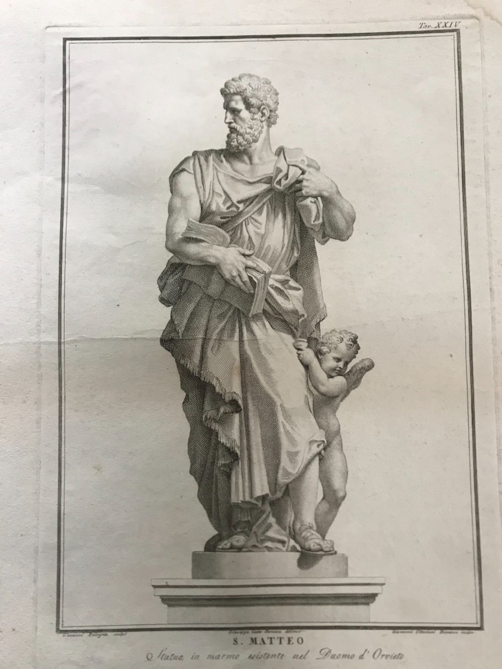 An 18th-century monochrome copperplate engraving depicting a classical draped statue of Saint Matthew holding a book alongside a winged cherub on a plinth.