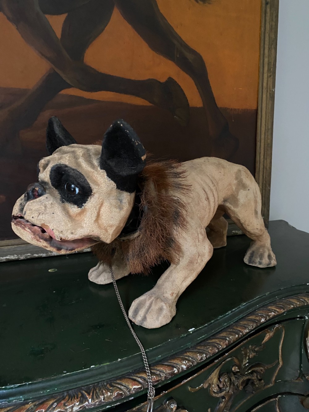 A 19th-century papier-mache French bulldog figure featuring painted cream skin, black eye patches, glass eyes, a dark fur collar, and a metal chain leash.