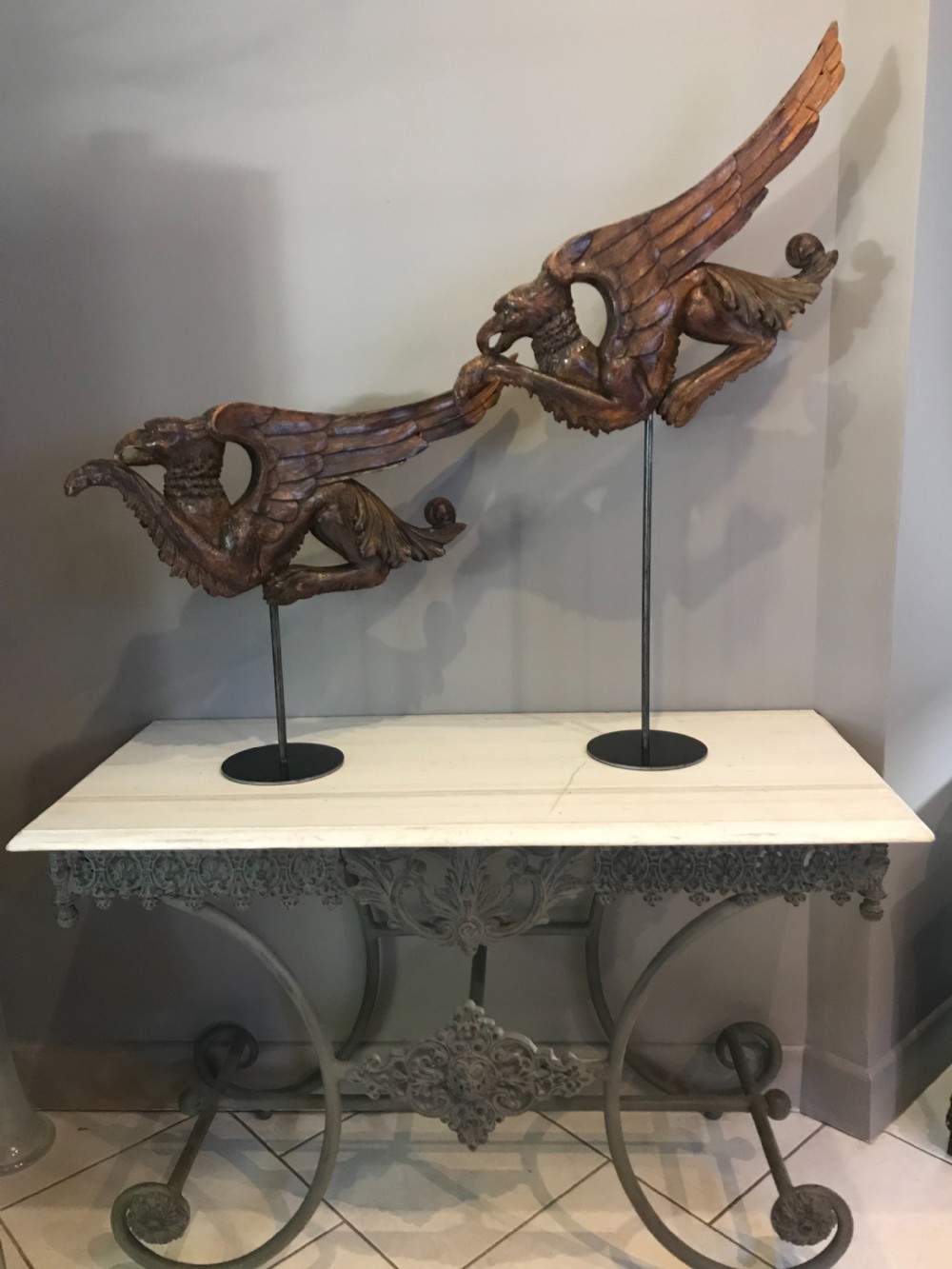 A pair of 19th-century carved walnut winged griffin sculptures mounted on slender dark metal display stands.