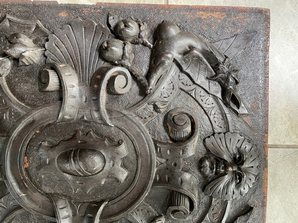 A rectangular dark walnut wood panel featuring high-relief carvings of a Green Man mask, mythical winged beasts, scrolls, and foliate motifs. View III