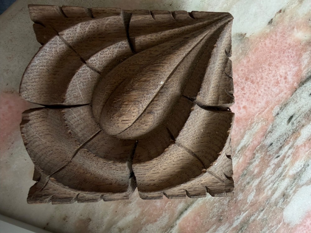 A square hand-carved oak panel featuring a central teardrop motif surrounded by concentric leaf relief carving.