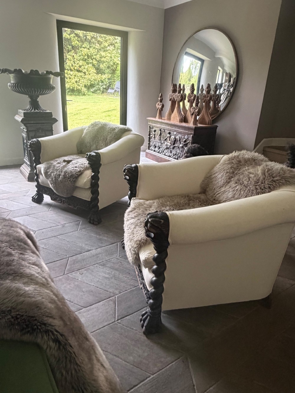 A pair of 19th-century armchairs featuring light cream upholstery and dark carved oak frames with barley twist pillars and lion head terminals.