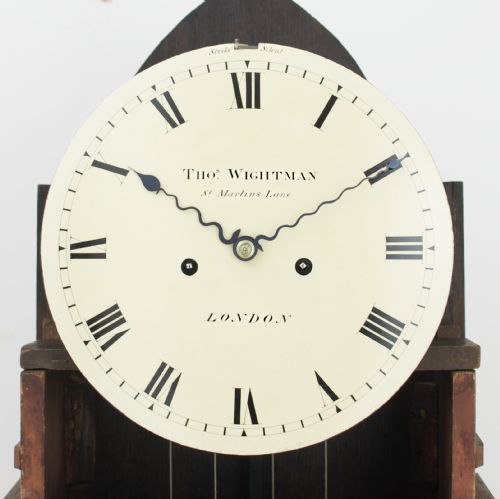 fig 3. A Regency flame mahogany longcase clock featuring a pointed arch hood, white circular dial signed by Thomas Wightman of London, and brass column details.